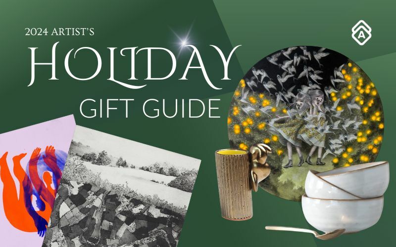 A holiday gift guide banner with a deep green background featuring the text "2024 ARTIST'S HOLIDAY GIFT GUIDE" in elegant white typography. The image displays various art pieces including an abstract red and blue artwork on pink paper, a black and white aerial landscape photograph, and a circular decorative plate featuring whimsical figures surrounded by golden lights. In the foreground are ceramic bowls with gold trim and what appears to be a gold-toned vessel. A white geometric logo appears in the top right corner. All artworks pictured are available in the Holiday Gift Guide.