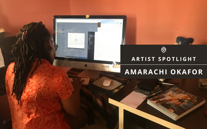 Artist Amarachi Okafor sits at her desk, working on Artwork Archive on a large computer monitor. She wears a patterned orange shirt and has long locks secured with a clip. The workspace includes notebooks, papers, and a pen. A black banner on the right side of the image reads 'Artist Spotlight: Amarachi Okafor.