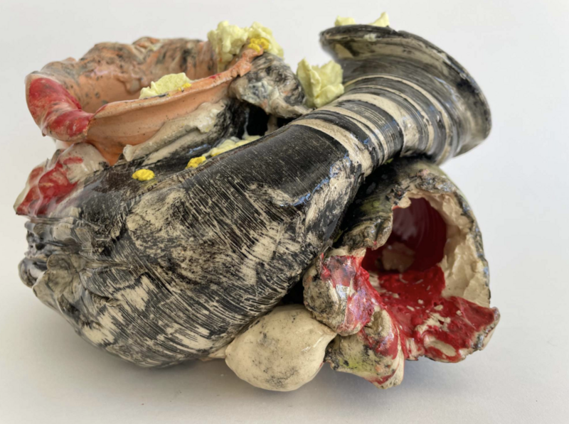 Abstract ceramic sculpture titled Remains #8 (2025) by Lynn Basa, measuring 6 x 9 x 9 inches. The twisted, contorted form incorporates glossy black and cream striations, ruptured red and beige interiors, and splashes of yellow and pale green.