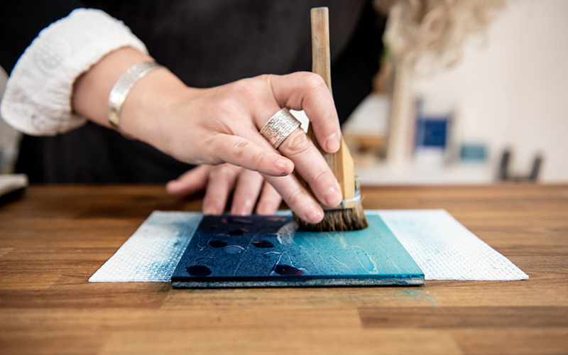 An artist uses paintbrush to apply pigment to a woodblock.