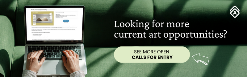 A person types on a laptop computer while seated on a green couch. The laptop screen displays an art opportunity listing titled "The Luminous Edge of Being." Their hands rest on the keyboard, wearing a striped long-sleeved shirt. The scene is photographed from above against plush green upholstery. White text on the right reads "Looking for more current art opportunities?" followed by a light green button stating "SEE MORE OPEN CALLS FOR ENTRY" with a hand-drawn arrow pointing to it. A small logo appears in the upper right corner. The image conveys artists actively searching for professional opportunities online.