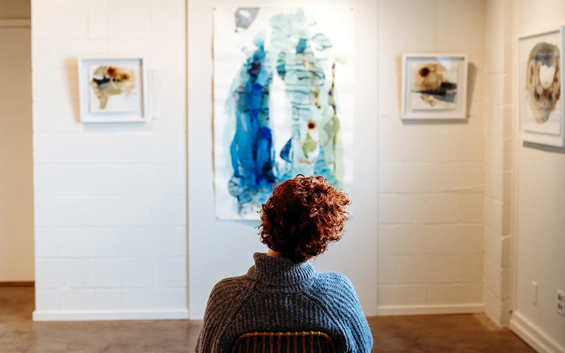 A woman sits in front of artworks in a gallery