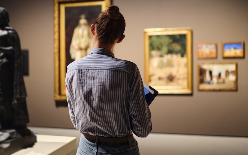 back view of a female visitor in art museum looking at art object 