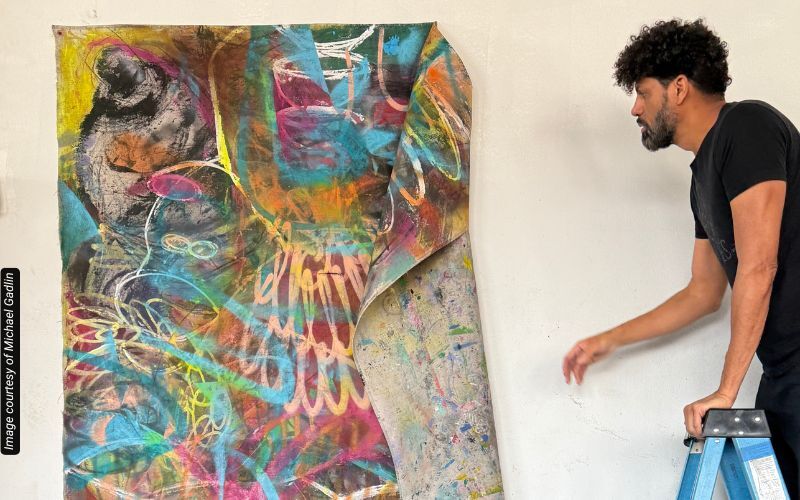 an artist on a ladder reaching for a colorful canvas