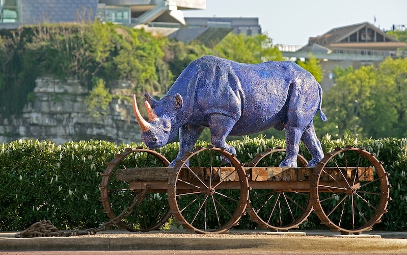 sculpture of a blue rhino on a wooden cart