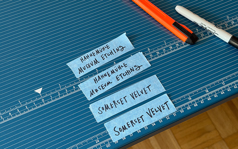 Tape strips with paper names written on them in marker, on top of self-healing cutting mats