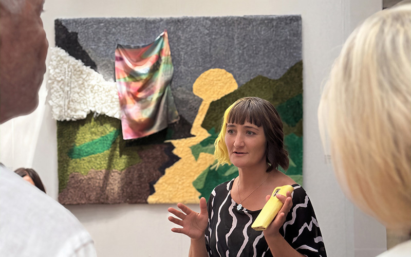 A woman standing in front of artworks speaking to a crowd