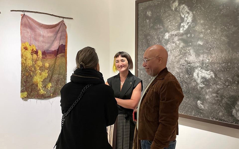 A woman speaks with two people in front of artworks